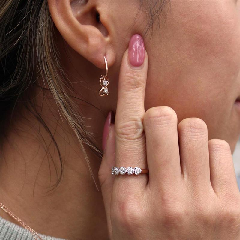 A woman holding her ear with her pointer finger to show our breathtaking heart shaped diamond earrings.