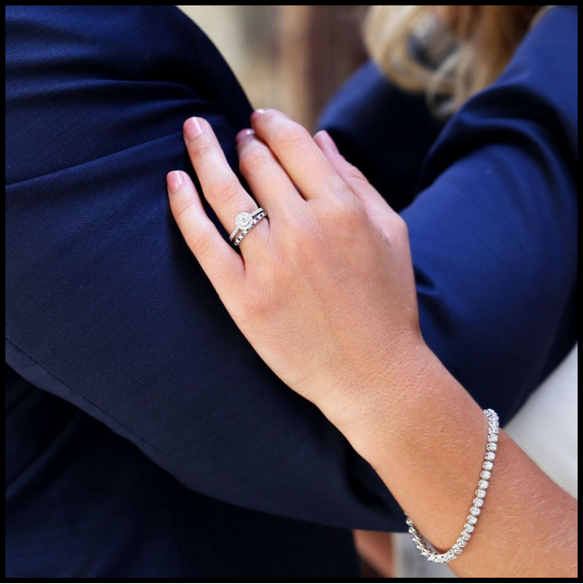 A woman's arm on a mans showcasing our glistening engagement ring and tennis bracelet.