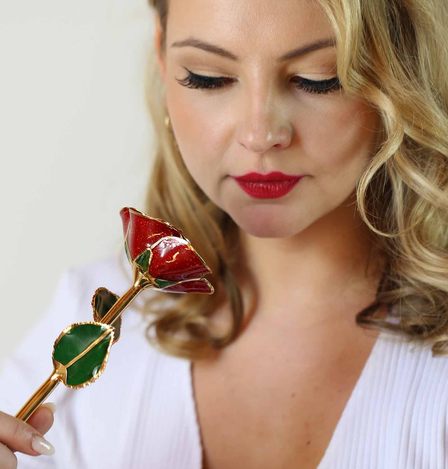 A woman with a red lip looking down at a classic red 24 karat gold dipped rose.