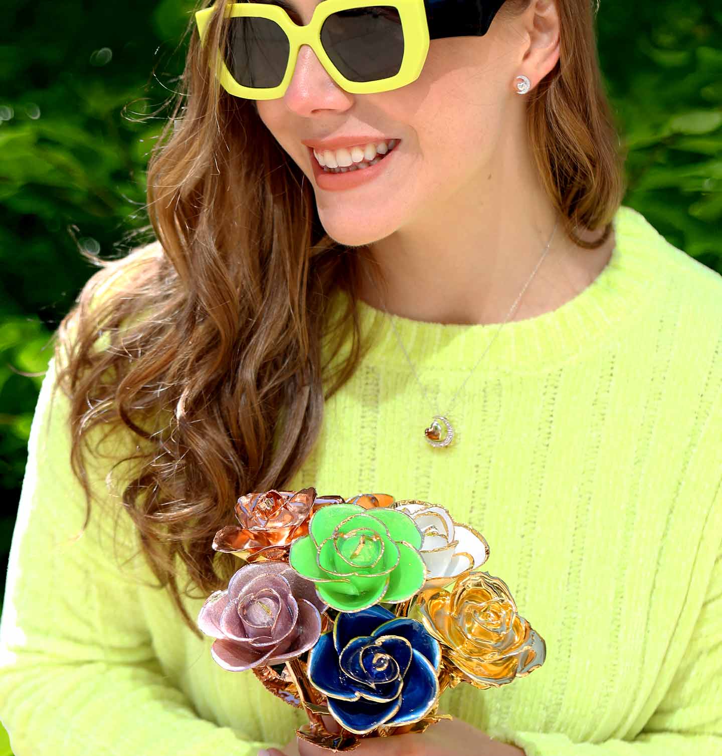 A girl in a neon shirt and glasses holding a bouquet of roses including white, green, classic gold, lilac, blue and rose gold dipped roses.